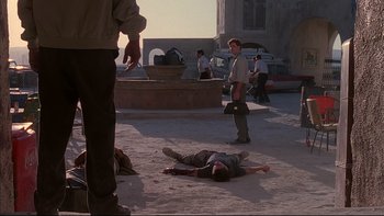 Movie still from “The Way of the Gun” (2000), directed by Christopher McQuarrie – A man laying on the ground in the middle of the street; Wide shot, Over the shoulder angle
