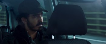 Movie still from “The Wedding Guest” (2018), directed by Michael Winterbottom – A man sitting in the back seat of a car; Close Up shot, Over the shoulder angle