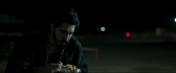 Movie still from “The Wedding Guest” (2018), directed by Michael Winterbottom – A man sitting at a table with a bowl of food; Close Up shot, Low angle