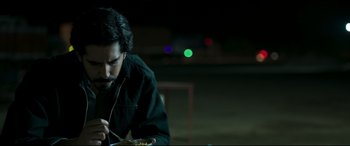 Movie still from “The Wedding Guest” (2018), directed by Michael Winterbottom – A man sitting at a table eating food; Medium shot, Over the shoulder angle