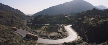 Movie still from “The Wedding Guest” (2018), directed by Michael Winterbottom – A road that has been shaped into a curve in the road; Extreme Wide shot, High angle