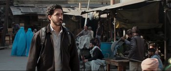 Movie still from “The Wedding Guest” (2018), directed by Michael Winterbottom – A man standing in front of a group of people; Medium shot, Over the shoulder angle