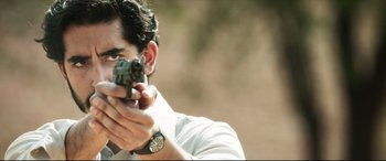Movie still from “The Wedding Guest” (2018), directed by Michael Winterbottom – A man holding a gun while wearing a white shirt; Close Up shot, Low angle