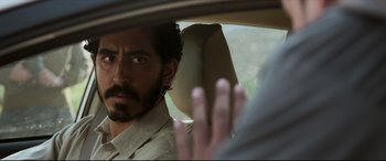 Movie still from “The Wedding Guest” (2018), directed by Michael Winterbottom – A person in a car looking at the camera; Close Up shot, Over the shoulder angle