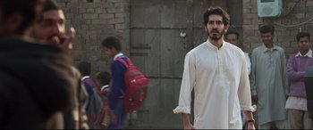 Movie still from “The Wedding Guest” (2018), directed by Michael Winterbottom – A man standing in front of a group of children; Medium shot, Low angle