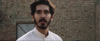 Movie still from “The Wedding Guest” (2018), directed by Michael Winterbottom – A person wearing a white shirt; Close Up shot, Over the shoulder angle