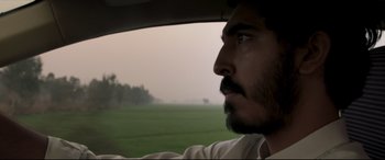 Movie still from “The Wedding Guest” (2018), directed by Michael Winterbottom – A man with a beard looking out of a car window; Close Up shot, Low angle