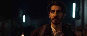 Movie still from “The Wedding Guest” (2018), directed by Michael Winterbottom – A person with a beard wearing a jacket; Close Up shot, Over the shoulder angle