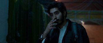 Movie still from “The Wedding Guest” (2018), directed by Michael Winterbottom – A man smoking a cigarette in a dark room; Close Up shot, Over the shoulder angle