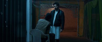 Movie still from “The Wedding Guest” (2018), directed by Michael Winterbottom – A man standing next to a chair in a room; Medium shot, Over the shoulder angle