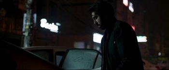 Movie still from “The Wedding Guest” (2018), directed by Michael Winterbottom – A man standing in front of a car at night; Medium shot, Low angle