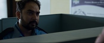 Movie still from “The Wedding Guest” (2018), directed by Michael Winterbottom – A person sitting at a desk; Close Up shot, Over the shoulder angle