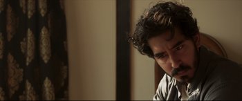 Movie still from “The Wedding Guest” (2018), directed by Michael Winterbottom – A man with curly hair is sitting down; Close Up shot, Over the shoulder angle