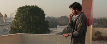 Movie still from “The Wedding Guest” (2018), directed by Michael Winterbottom – A man standing on top of a building talking on a cell phone; Medium shot, Low angle