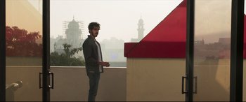 Movie still from “The Wedding Guest” (2018), directed by Michael Winterbottom – A man standing next to a building on top of a building; Wide shot, Low angle