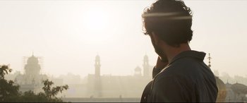Movie still from “The Wedding Guest” (2018), directed by Michael Winterbottom – A man standing in front of a large building; Close Up shot, Low angle