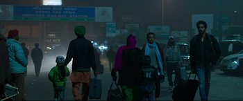 Movie still from “The Wedding Guest” (2018), directed by Michael Winterbottom – A group of people walking down a street at night; Wide shot, Low angle