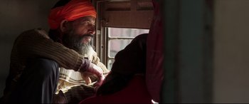 Movie still from “The Wedding Guest” (2018), directed by Michael Winterbottom – A man with a beard and a orange hat; Close Up shot, High angle