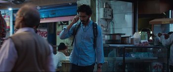 Movie still from “The Wedding Guest” (2018), directed by Michael Winterbottom – A man with a backpack talking on a cell phone; Medium shot, Over the shoulder angle