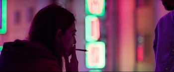 Movie still from “The Wedding Guest” (2018), directed by Michael Winterbottom – A woman is smoking a cigarette in front of a neon sign; Close Up shot, Over the shoulder angle