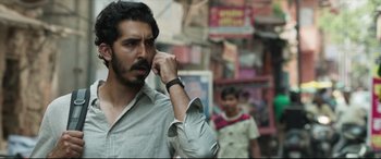 Movie still from “The Wedding Guest” (2018), directed by Michael Winterbottom – A man talking on a cell phone while walking down a street; Close Up shot, Over the shoulder angle
