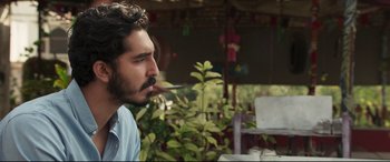 Movie still from “The Wedding Guest” (2018), directed by Michael Winterbottom – A man smoking a cigarette while sitting in a chair; Close Up shot, Over the shoulder angle