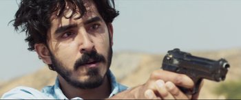 Movie still from “The Wedding Guest” (2018), directed by Michael Winterbottom – A person holding a gun; Close Up shot, Over the shoulder angle