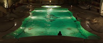 Movie still from “The Wedding Guest” (2018), directed by Michael Winterbottom – A person sitting in a pool at night with lights on; Extreme Wide shot, High angle