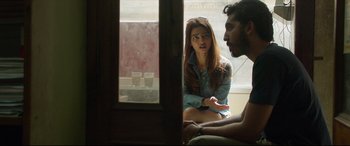 Movie still from “The Wedding Guest” (2018), directed by Michael Winterbottom – A woman sitting next to a man in front of a window; Medium shot, Over the shoulder angle