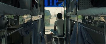 Movie still from “The Wedding Guest” (2018), directed by Michael Winterbottom – A man sitting on a chair on a bus; Medium shot, Low angle
