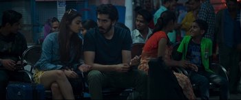 Movie still from “The Wedding Guest” (2018), directed by Michael Winterbottom – A group of people sitting in a room; Medium shot, Over the shoulder angle