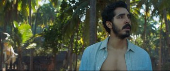 Movie still from “The Wedding Guest” (2018), directed by Michael Winterbottom – A man with a beard is standing in front of trees; Close Up shot, Over the shoulder angle
