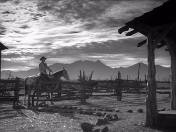 Movie still from “The Westerner” (1940), directed by William Wyler – A man riding a horse in a field with mountains in the background; Wide shot, Low angle