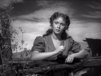 Movie still from “The Westerner” (1940), directed by William Wyler – A black - and - white photo of a woman leaning on a fence; Medium shot, Low angle