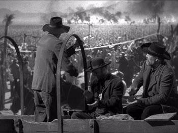 Movie still from “The Westerner” (1940), directed by William Wyler – A black and white photo of men sitting in front of a crowd; Wide shot, High angle