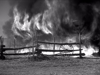 Movie still from “The Westerner” (1940), directed by William Wyler – An old wagon wheel sitting in front of a burning fence; Extreme Wide shot, Low angle