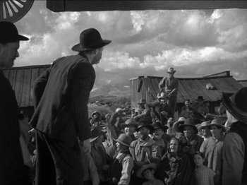 Movie still from “The Westerner” (1940), directed by William Wyler – An old photo of a crowd of people watching a man on a stage; Wide shot, Low angle