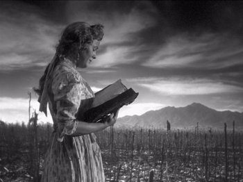 Movie still from “The Westerner” (1940), directed by William Wyler – A woman standing in the middle of a field holding an open book; Medium shot, Low angle