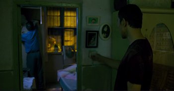 Movie still from “The Wild Goose Lake” (2019), directed by Yi'nan Diao – A man standing next to a bed in a room; Medium shot, Over the shoulder angle