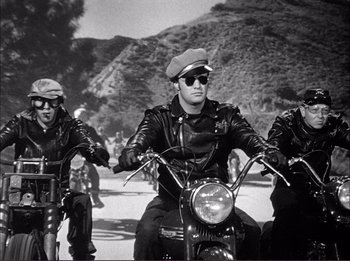 Movie still from “The Wild One” (1953), directed by Laslo Benedek – A group of men riding motorcycles down a street; Medium shot, Low angle