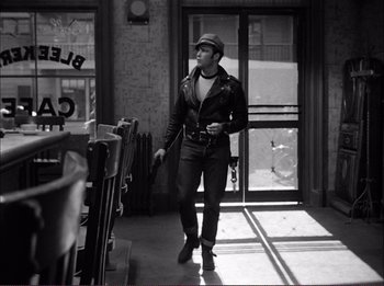 Movie still from “The Wild One” (1953), directed by Laslo Benedek – A man in a leather jacket walking through a building; Medium shot, Low angle