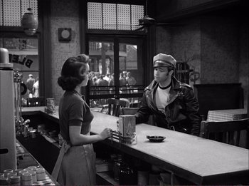 Movie still from “The Wild One” (1953), directed by Laslo Benedek – A woman standing at a counter talking to a man; Medium shot, Over the shoulder angle