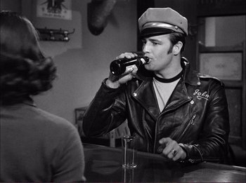 Movie still from “The Wild One” (1953), directed by Laslo Benedek – A man in a leather jacket drinking a beer; Medium shot, Over the shoulder angle
