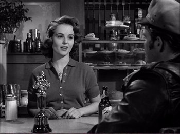 Movie still from “The Wild One” (1953), directed by Laslo Benedek – A woman sitting at a table in a restaurant; Medium shot, Over the shoulder angle