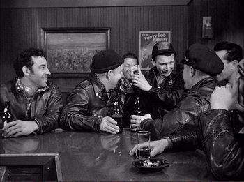 Movie still from “The Wild One” (1953), directed by Laslo Benedek – A black and white photo of a group of men sitting at a table drinking beer; Medium shot, High angle