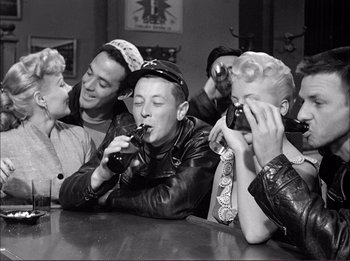 Movie still from “The Wild One” (1953), directed by Laslo Benedek – A group of people sitting at a table drinking soda; Medium shot, High angle