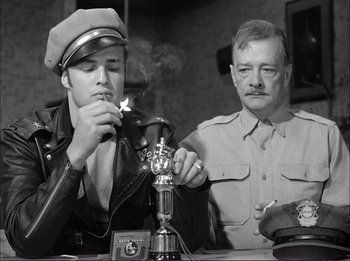 Movie still from “The Wild One” (1953), directed by Laslo Benedek – A man smoking a cigarette next to another man; Medium shot, Low angle