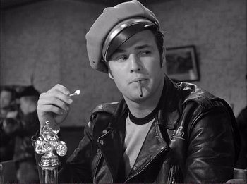 Movie still from “The Wild One” (1953), directed by Laslo Benedek – A man in a leather jacket and hat smoking a cigarette; Close Up shot, Low angle