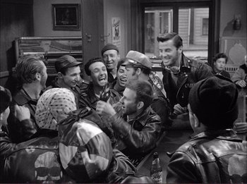 Movie still from “The Wild One” (1953), directed by Laslo Benedek – A group of men sitting around each other laughing; Medium shot, High angle