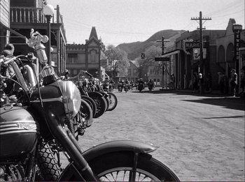 Movie still from “The Wild One” (1953), directed by Laslo Benedek – A row of motorcycles parked on the side of the street; Wide shot, Low angle